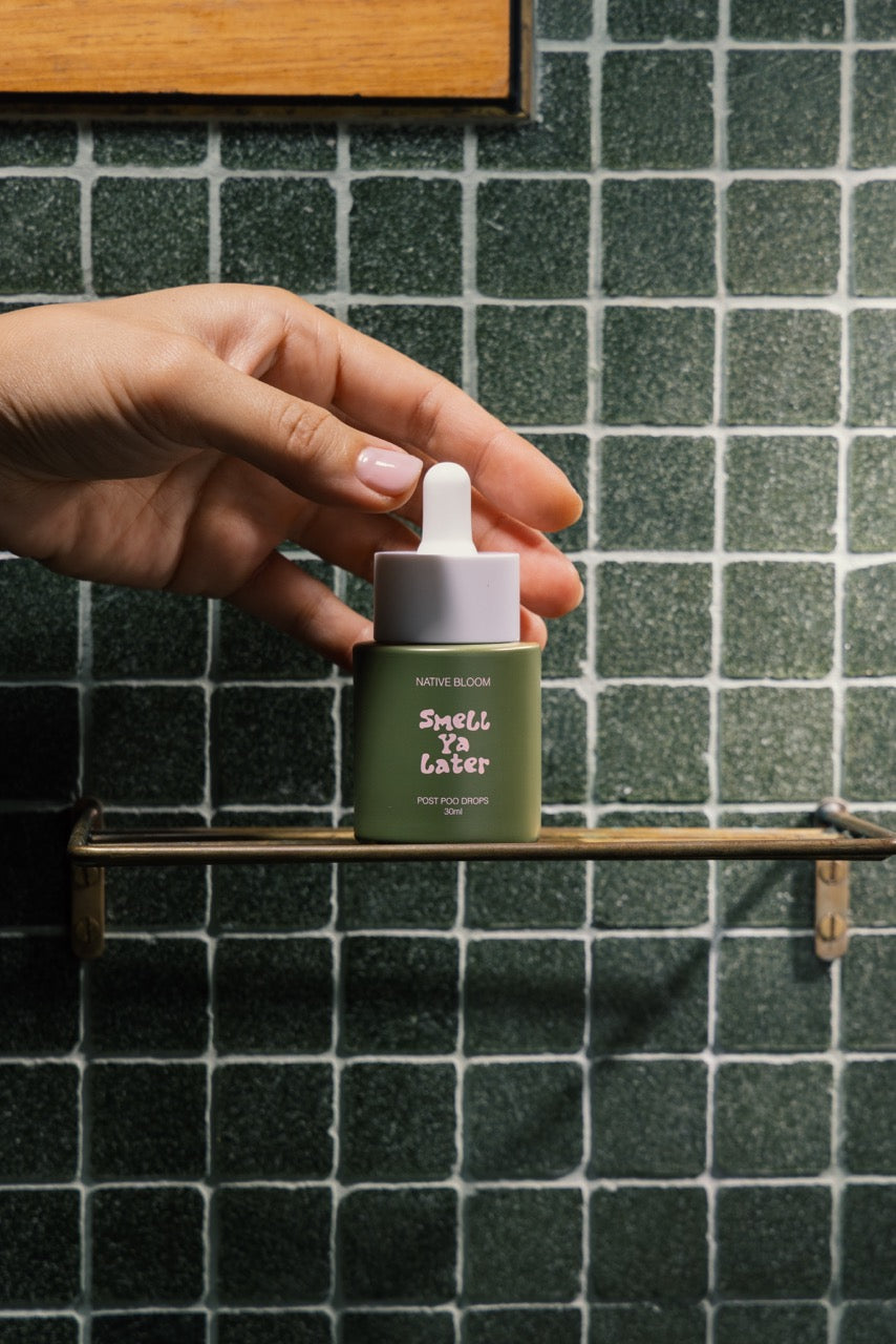 Hand holding a green dropper bottle labeled 'Smell Ya Laterr' against a tiled wall background